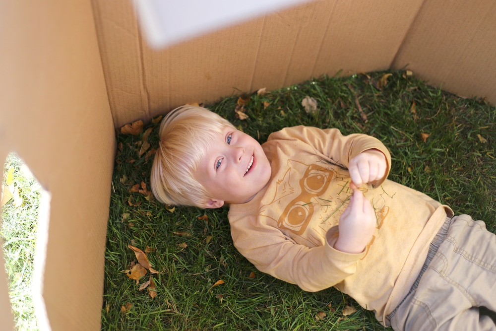 a kid in a cardboard fort outside