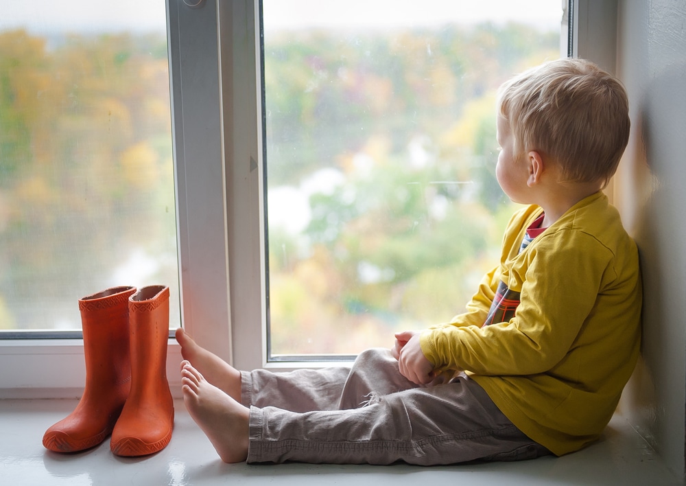 Little boy staring out window while it rains