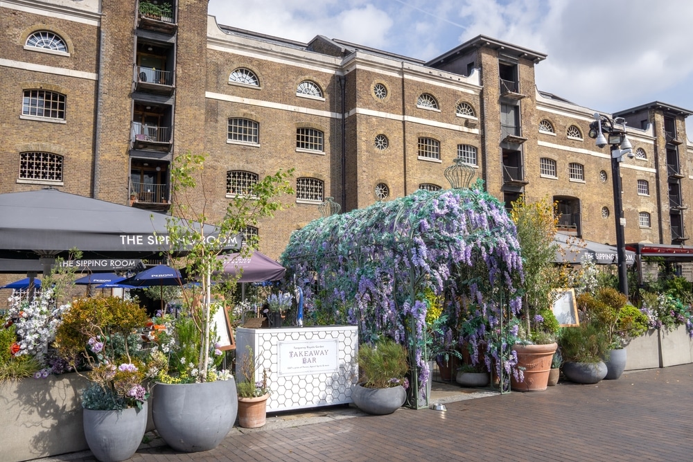 picture of the outside of the sipping room, with flowers at the entrance and tables
