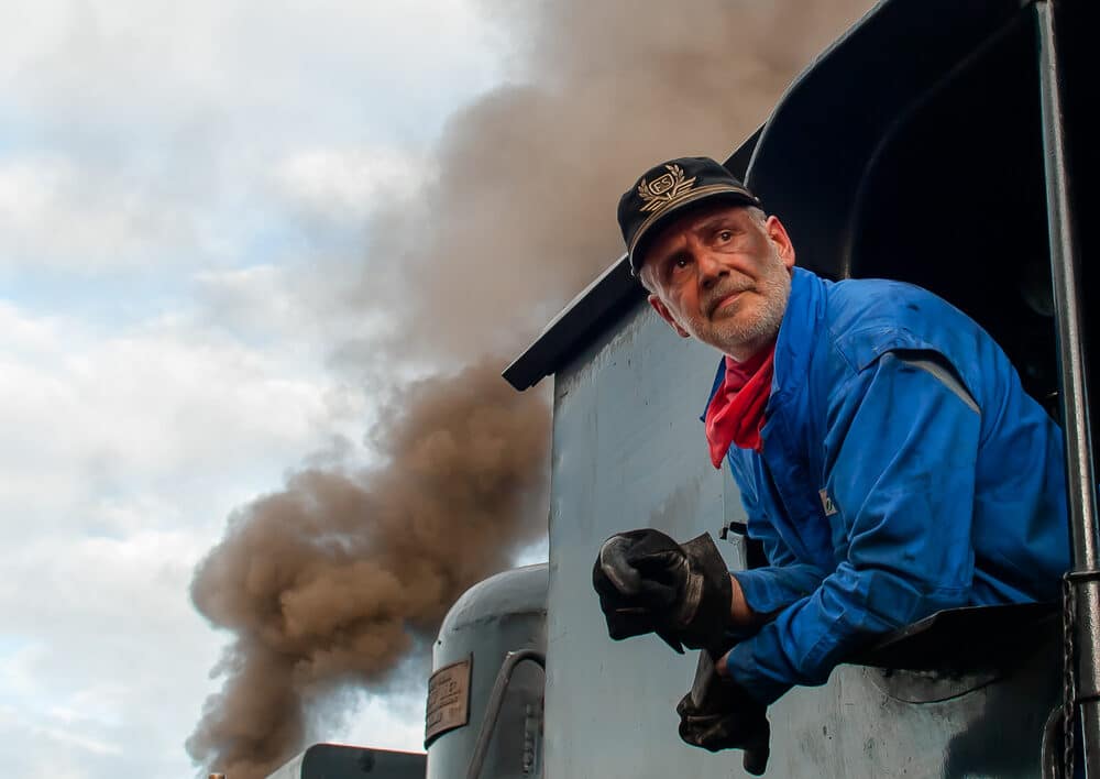 train driver outside steam train window with smoke in the background