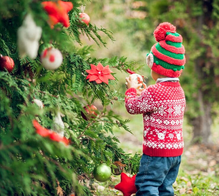 child wearing a christmas jumper decorating a tree