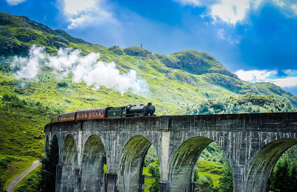 steam train travelling along bridge with mountains behind
