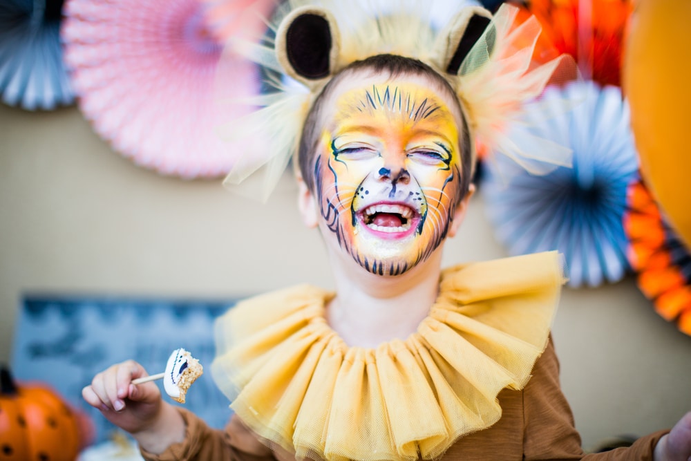 child dressed up as a lion with fluffy ears and a painted lion face too