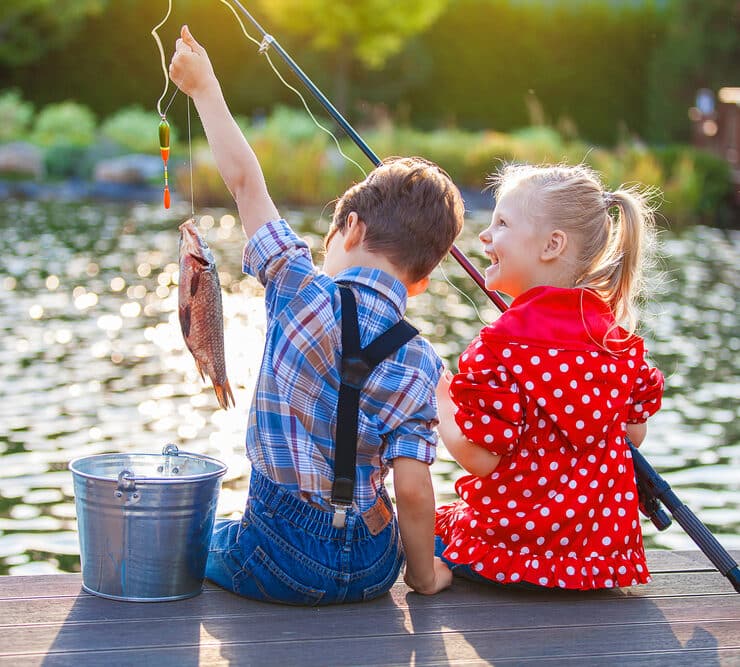 two kids sitting on a pier fishing in a lake