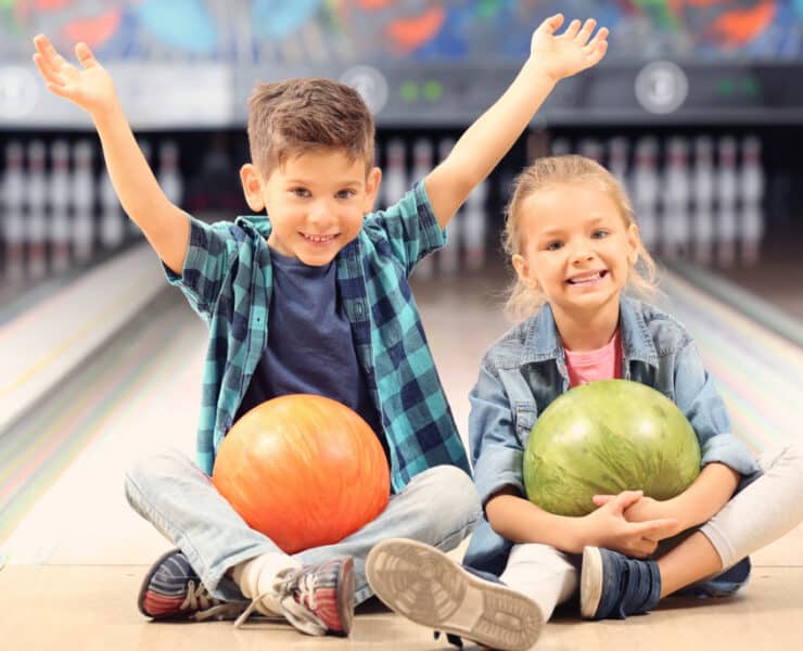 two kids sitting on the floor with bowling balls