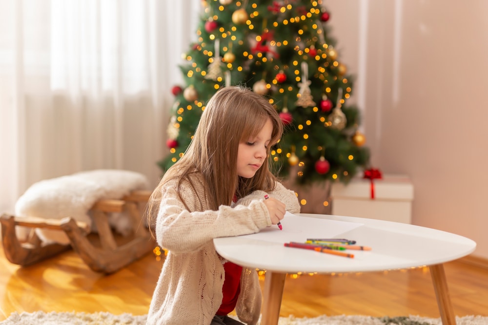 little girl colouring in by a christmas tree