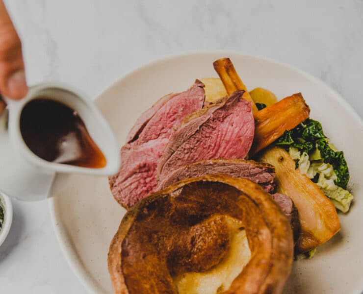 someone pouring gravy on a sunday roast dinner