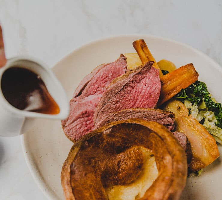 someone pouring gravy on a sunday roast dinner
