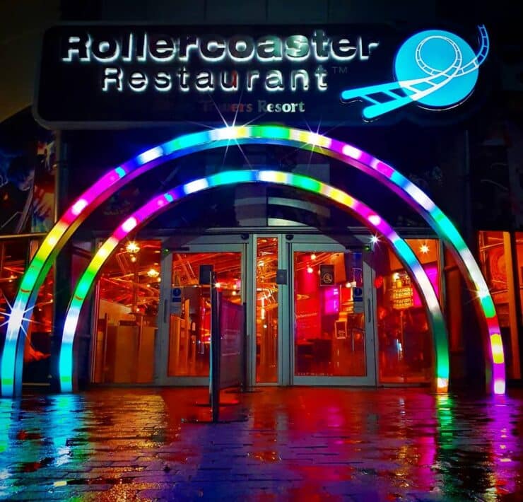 rollercoaster restaurant entrance lit up in multicoloured lights at night time.