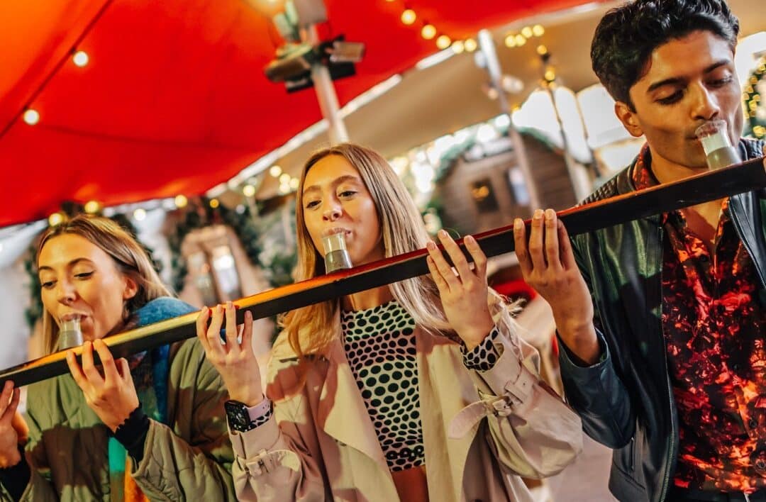 three young adults doing shots off a wooden ski