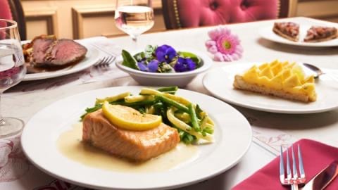 salmon, green and yellow beans, steak and cakes on a table decorated with flowers