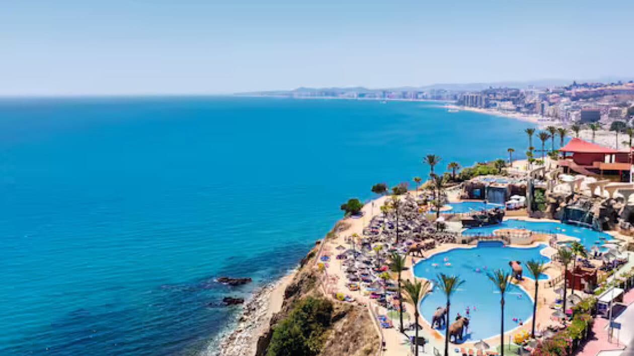 birds eye view of ocean next to a resort with palm trees and a pool