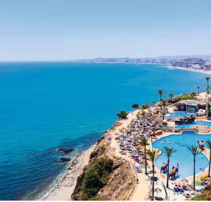 birds eye view of ocean next to a resort with palm trees and a pool
