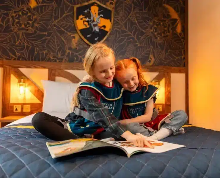 A family smiling and celebrating in front of a colorful castle, likely at a Merlin resort, during the Merlin Summer of Stays Competition.