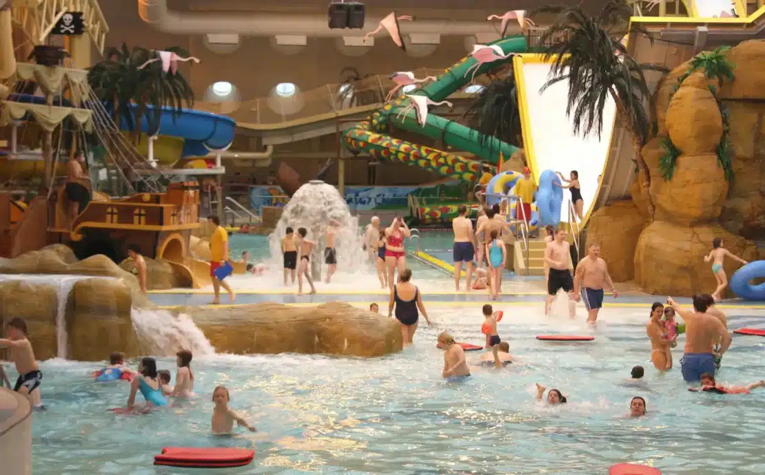 A wide, general view of the bustling Sandcastle Waterpark Blackpool, showing multiple slides, pools, and people enjoying the water attractions under the distinctive curved roof.