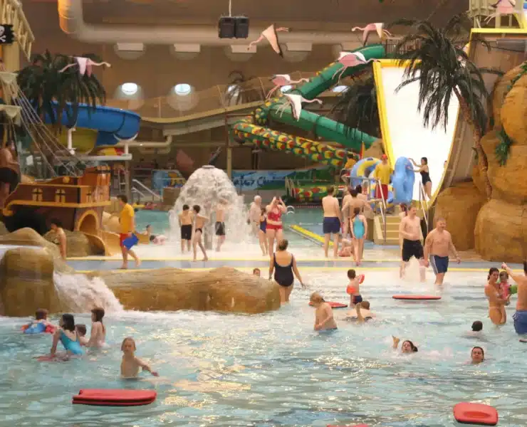 A wide, general view of the bustling Sandcastle Waterpark Blackpool, showing multiple slides, pools, and people enjoying the water attractions under the distinctive curved roof.