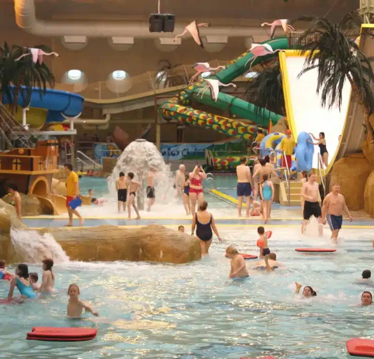 A wide, general view of the bustling Sandcastle Waterpark Blackpool, showing multiple slides, pools, and people enjoying the water attractions under the distinctive curved roof.