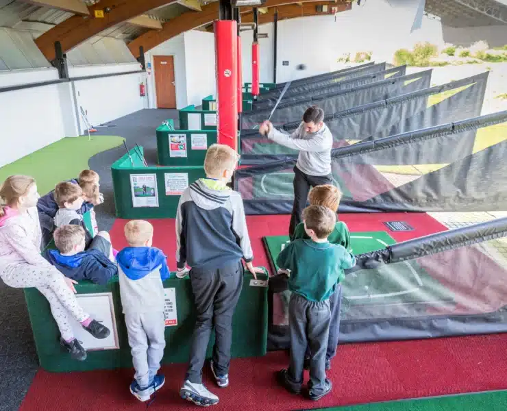 A family of four, including two young children, playing miniature golf at Dino Falls Adventure Golf with a large dinosaur model in the background.