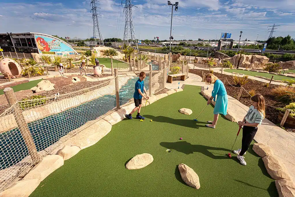 A close-up view of a golf ball about to be putted towards a hole at Dino Falls Adventure Golf, with part of a dinosaur visible in the blurred background.