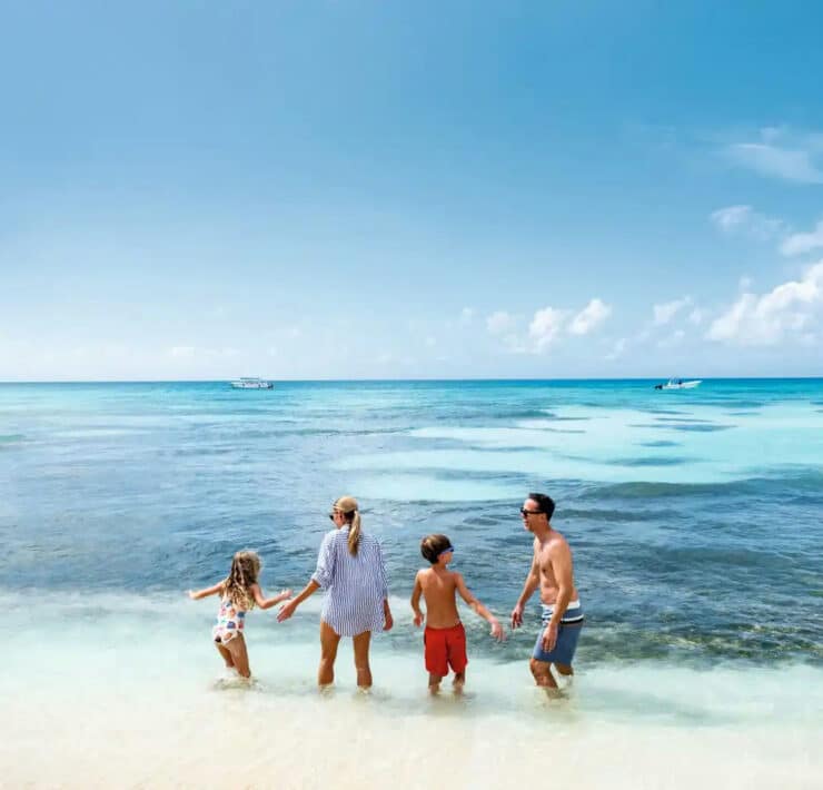 A family of four stands in the shallow, turquoise waters of a sunny beach in the Dominican Republic