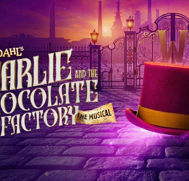 Oompa Loompas in vibrant orange costumes perform on stage for Charlie and the Chocolate Factory The Musical.